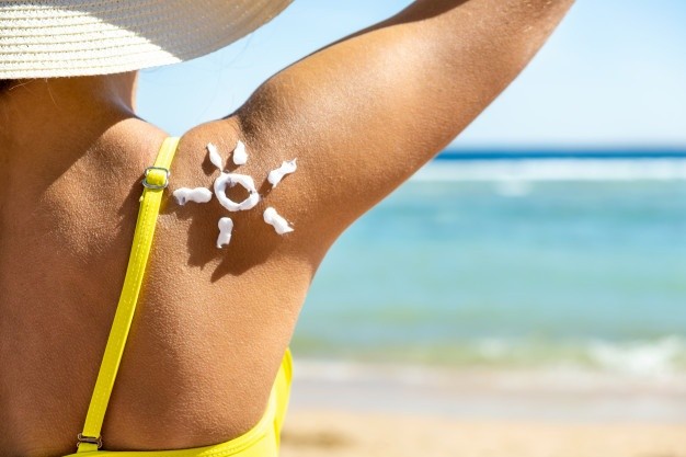 female wearing a hat on a sunny beach with sunscreen cream